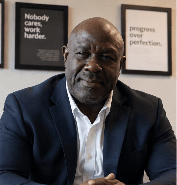 Confident Black man in a navy suit sitting before motivational posters in an office.